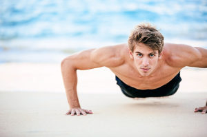 Fitness man doing push-ups on the beach. Male athlete exercising outdoors. Sports and active lifestyle.